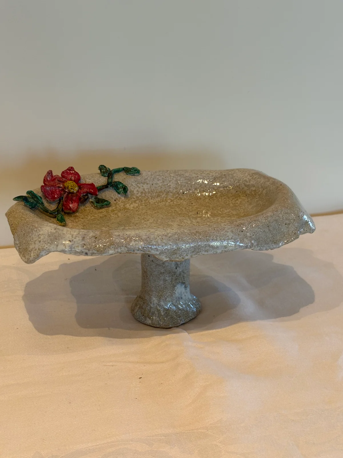 Avlangt beigespraglet fat med lite blomstermotiv festet. Liten pidestall.